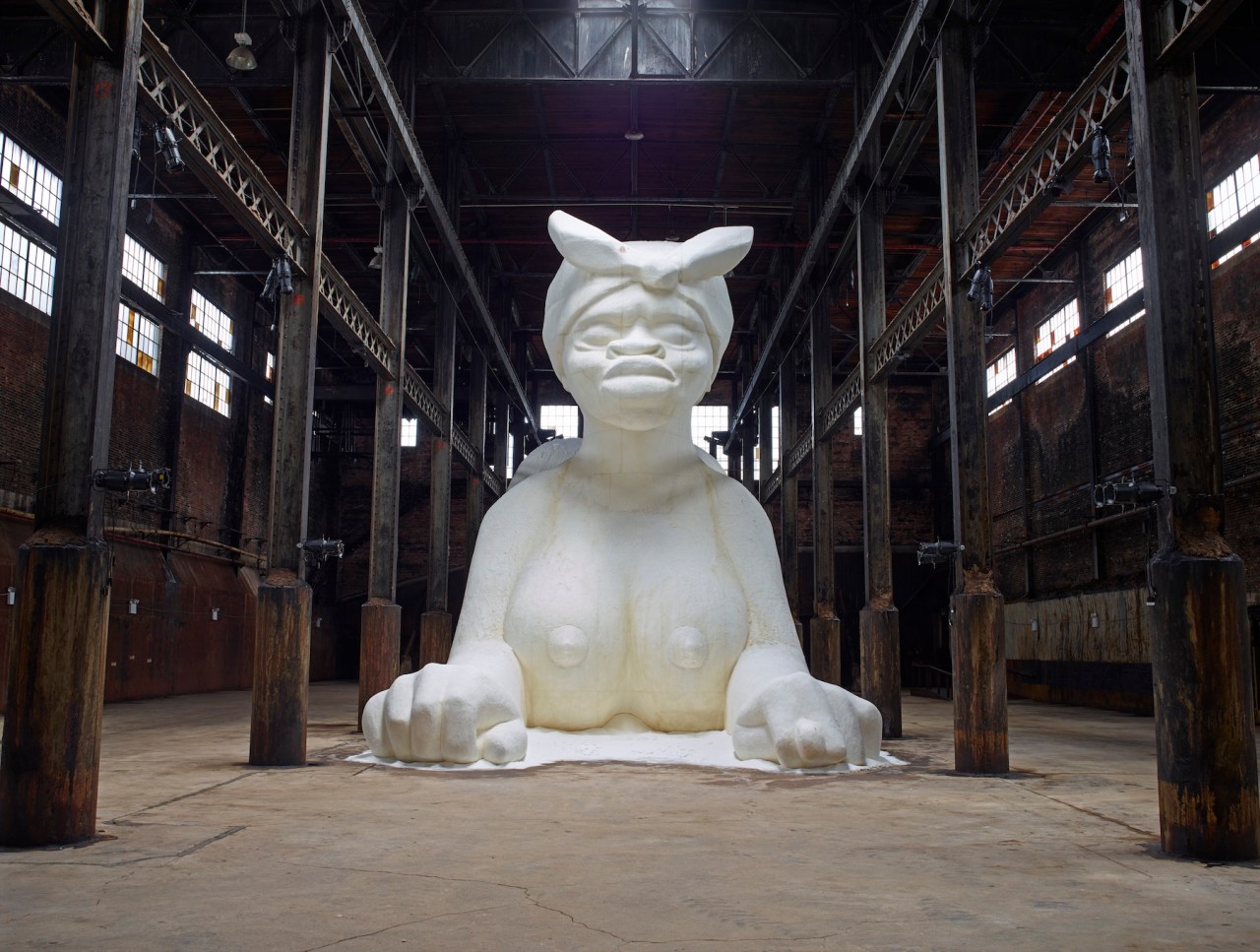 カラ・ウォーカー《A Subtlety, or the Marvelous Sugar Baby, an Homage to the unpaid and overworked Artisans who have refined our Sweet tastes from the cane fields to the Kitchens of the New World on the Occasion of the demolition of the Domino Sugar Refining Plant》（2014）。ニューヨーク、ブルックリンのドミノ製糖工場での展示風景。Photo: A project of Creative Time, Brooklyn, New York, 2014. Artwork copyright © 2014 Kara Walker, courtesy of Sikkema Malloy Jenkins and Sprüth Magers. Photo: Jason Wyche